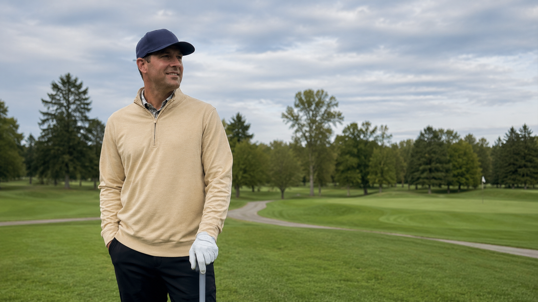 Golfer in a tan quarter-zip pullover and navy cap standing on the fairway on a cool, overcast morning